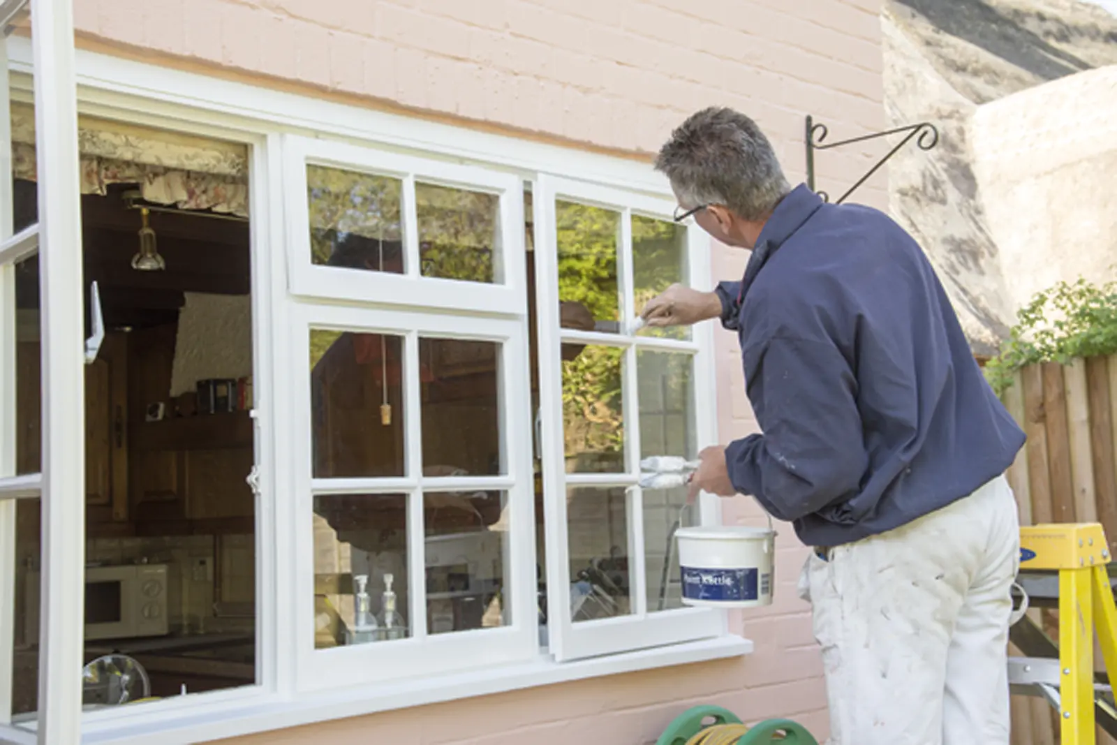 Decorator painting a white window frame as part of NVQ Assessment
