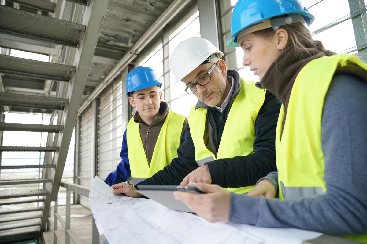 Construction supervisor reviewing drawings and a tablet with two colleagues